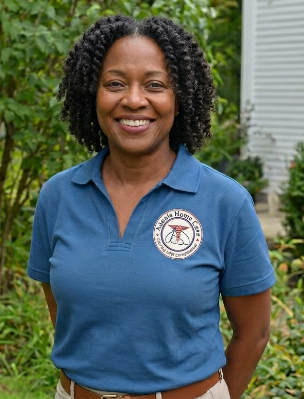 A female care giver stands smiling with her arms behind her back.